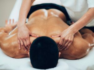 A therapist providing a deep tissue back massage to a patient on a folding treatment table, showcasing its versatility for therapy and sports medicine.
