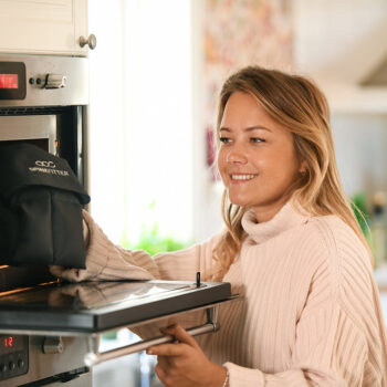 Woman placing the Sissel Spinefitter Linum Hot/Cold Pillow in an oven for heat therapy preparation.