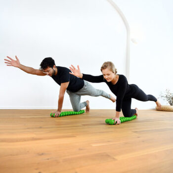 Man and woman balancing on their knees on the Sissel Spinefitter, raising arms for coordination training
