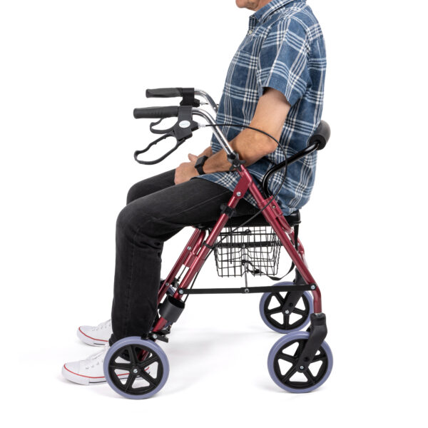Person seated on the padded seat of the rollator, using backrest for support.