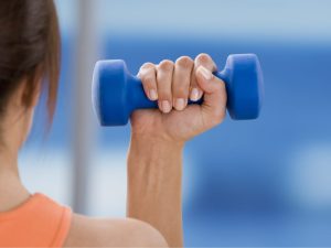 Close-up of a woman lifting a blue free weight, highlighting the benefits of weighted exercises for building strength, endurance, and weight loss