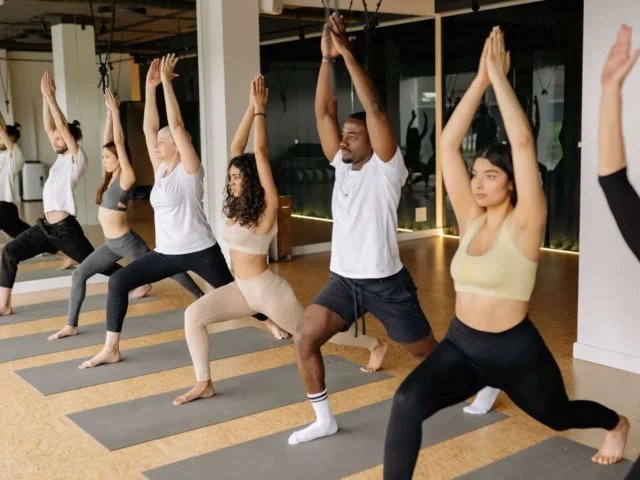 A yoga studio with over ten people practicing yoga on their yoga mats, following an instructor.