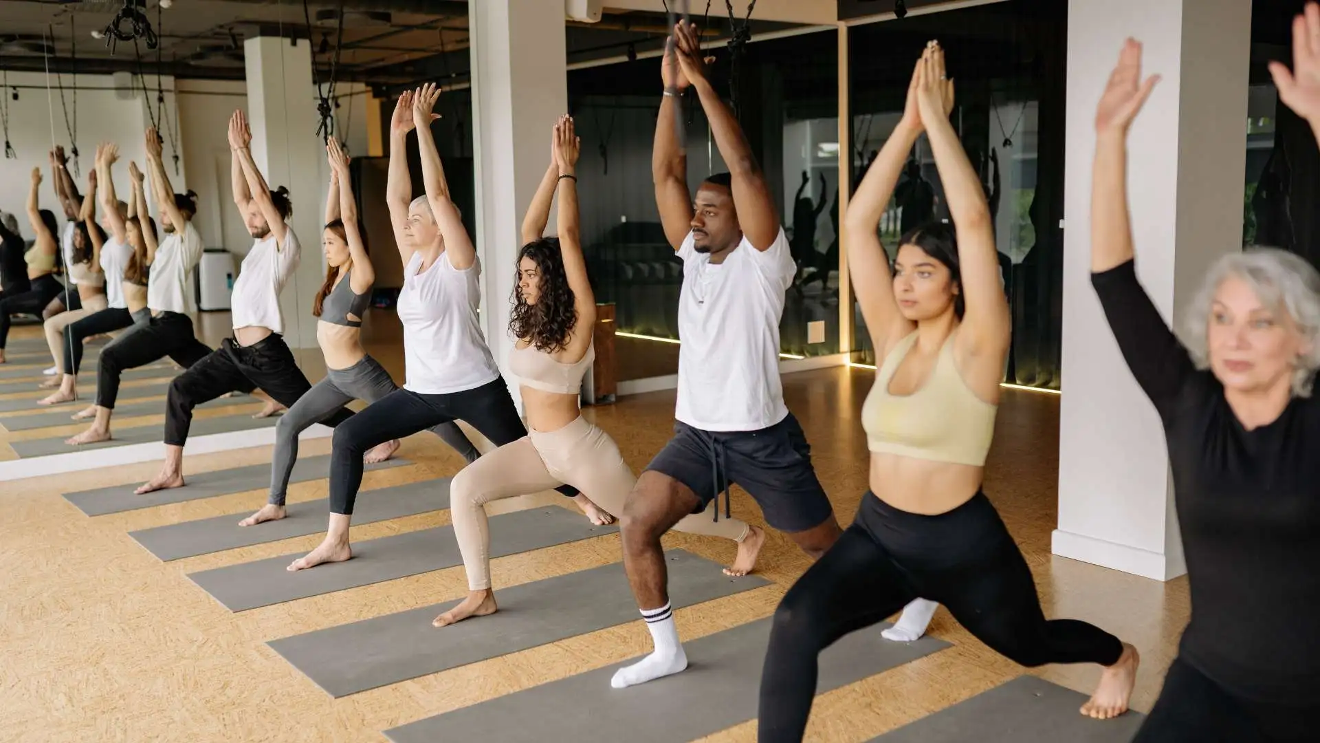 A yoga studio with over ten people practicing yoga on their yoga mats, following an instructor.