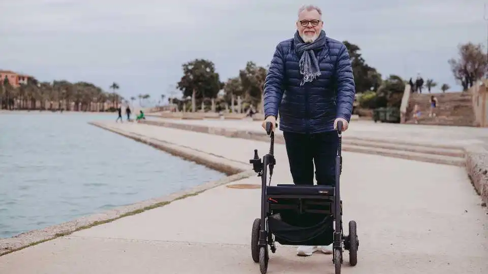 Elderly male walking using a 4-wheel rollator walker at the docks near the water. He is happy and independent.