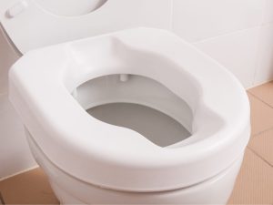 A white toilet seat riser installed on a standard toilet, designed for accessibility and comfort for elderly and disabled users