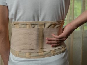 A person wearing a back brace for lifting weights, designed for support with conditions like osteoporosis and scoliosis, promoting better posture and back health.