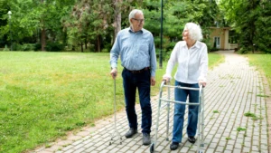 Elderly couple walkign in the park. The man is using a walking stick for walking support.