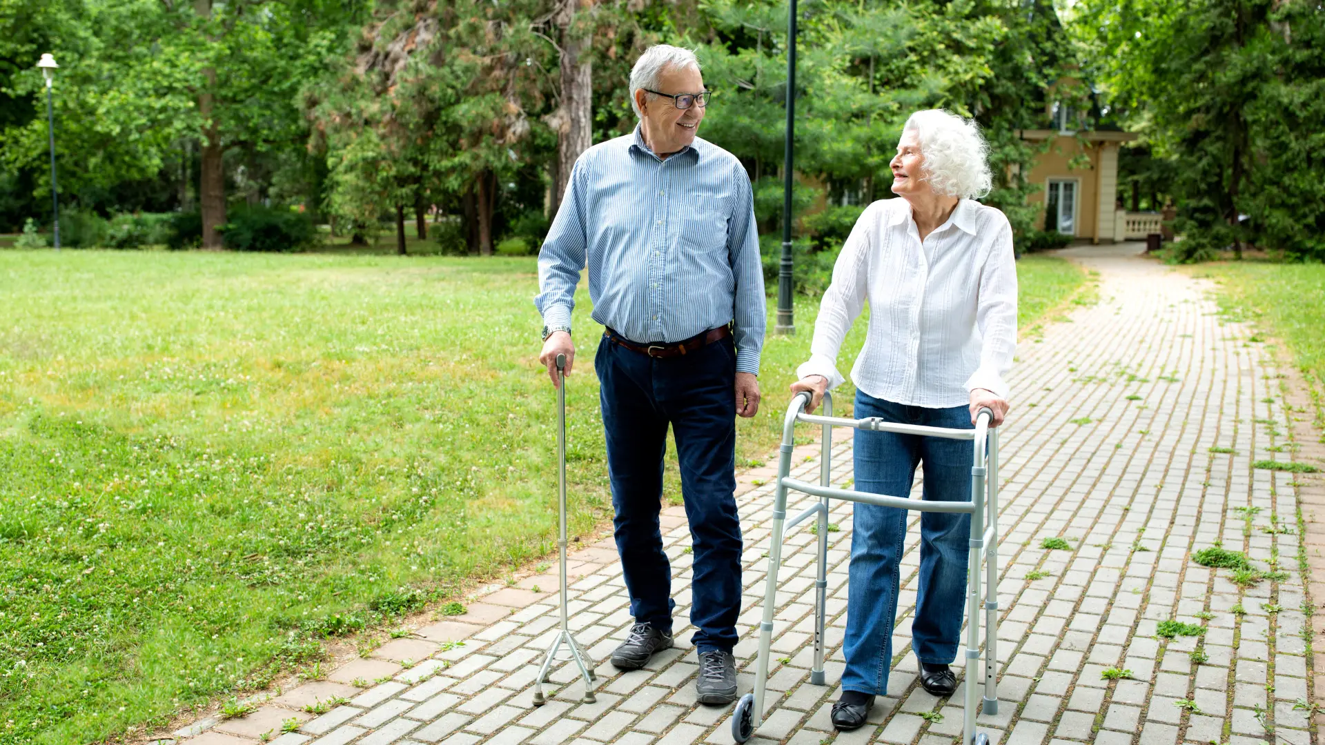 Elderly couple walkign in the park. The man is using a walking stick for walking support.