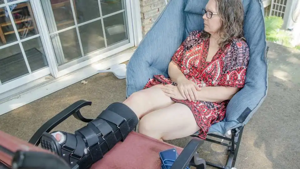 Woman wearing an orthopaedic boot on her right leg while napping on the garden chair.