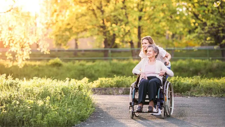 Woman pushing her elderly mom's wheelchair in the park.