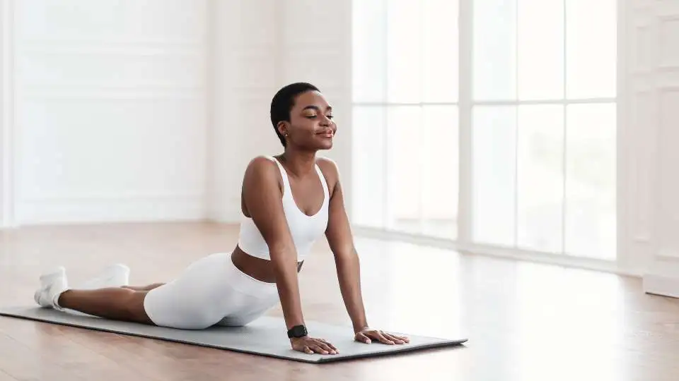 Young woman practicing yoga on a pink yoga mat. She is stretching her back.