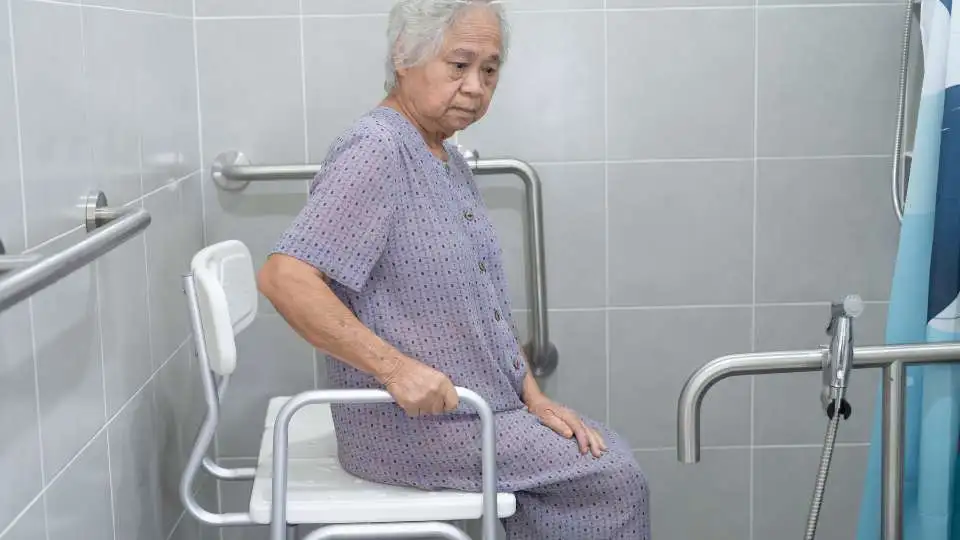Elderly lady using a shower chair with armrests and backrests provided by the HSE.