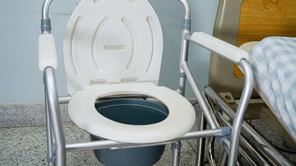 white commode chair with silver frame placed next to a bed.