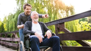 Young male helping his elderly father to push a bariatric wheelchair in the park.
