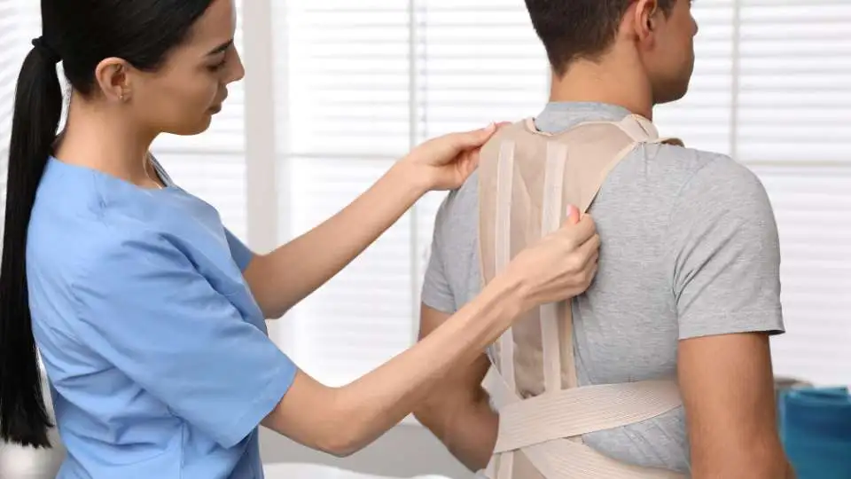 A physio helps a patient to put on a posture corrector the right way.