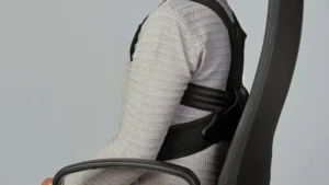 Male sitting on a chair with a straightened back wearing a posture corrector.