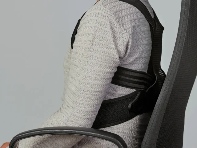 Male sitting on a chair with a straightened back wearing a posture corrector.
