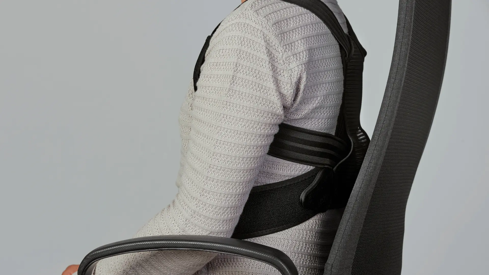 Male sitting on a chair with a straightened back wearing a posture corrector.