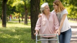 Woman hugging her elderly mother while she walks using a zimmer frame in the park.