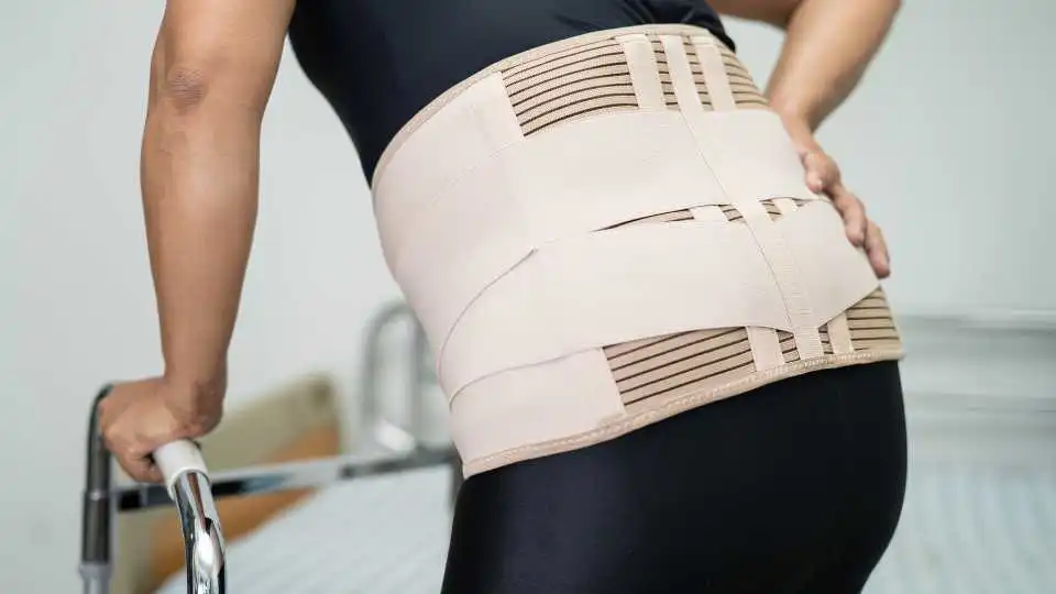 Elderly woman using a lower back support belt while walking.