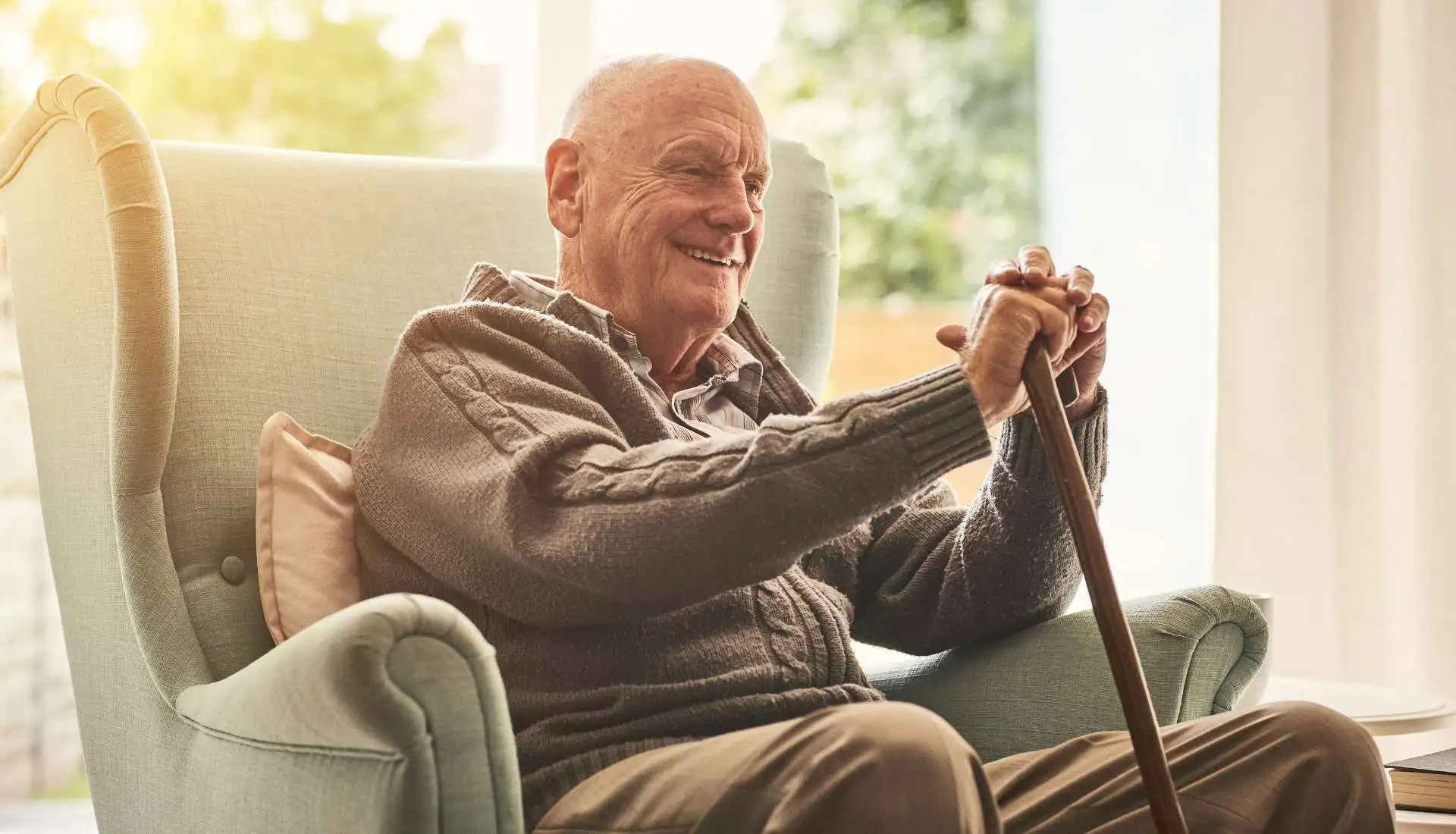 Elderly person with reduced mobility sitting on a chair while holding his walking stick.
