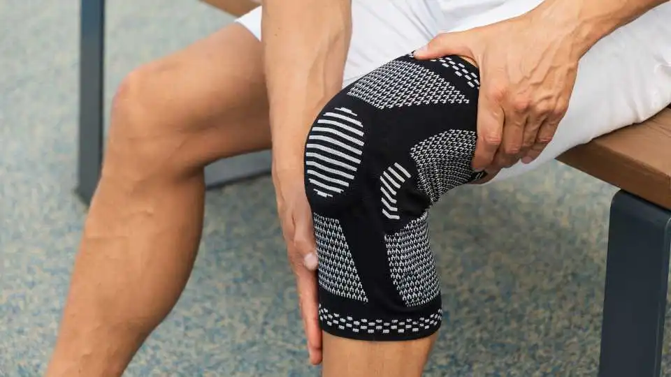 Mid age athlete wearing black elastic knee support on his left leg to manage his swelling around the knee.