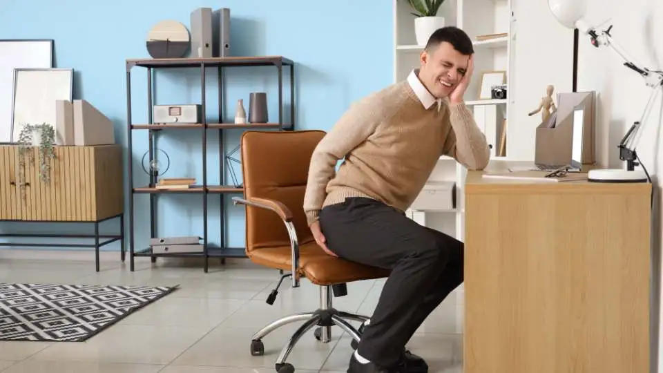 young man with haemorrhoids epxeriencing severe pain and looking for a donut cushion to be able to sit comfortably.