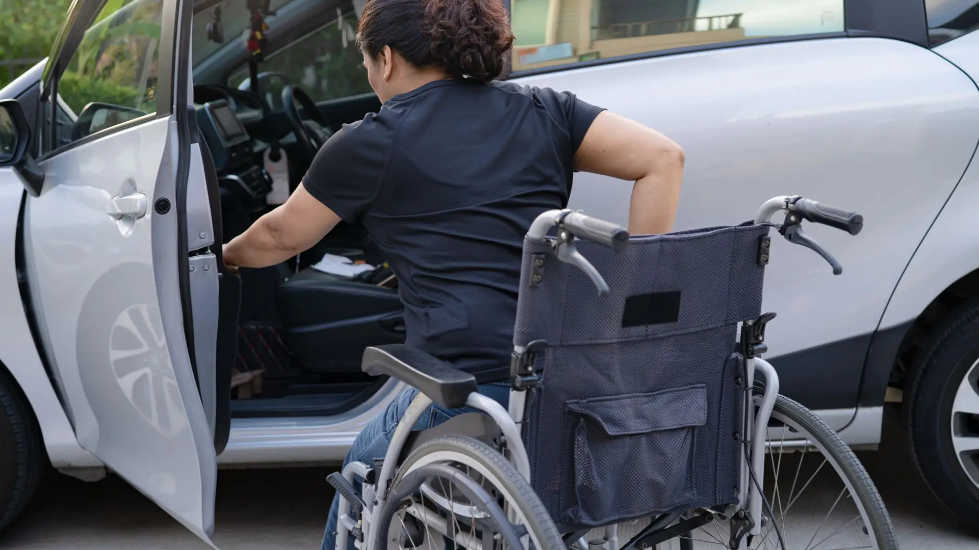 A female attempting to put her folding wheelchair in the car.