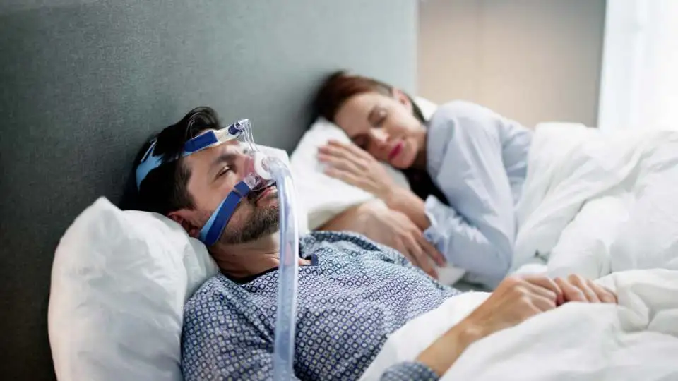 A man with sleep apnea wearing a CPAP mask and using a sleep apnea pillow as he is a back sleeper, to keep his head up.