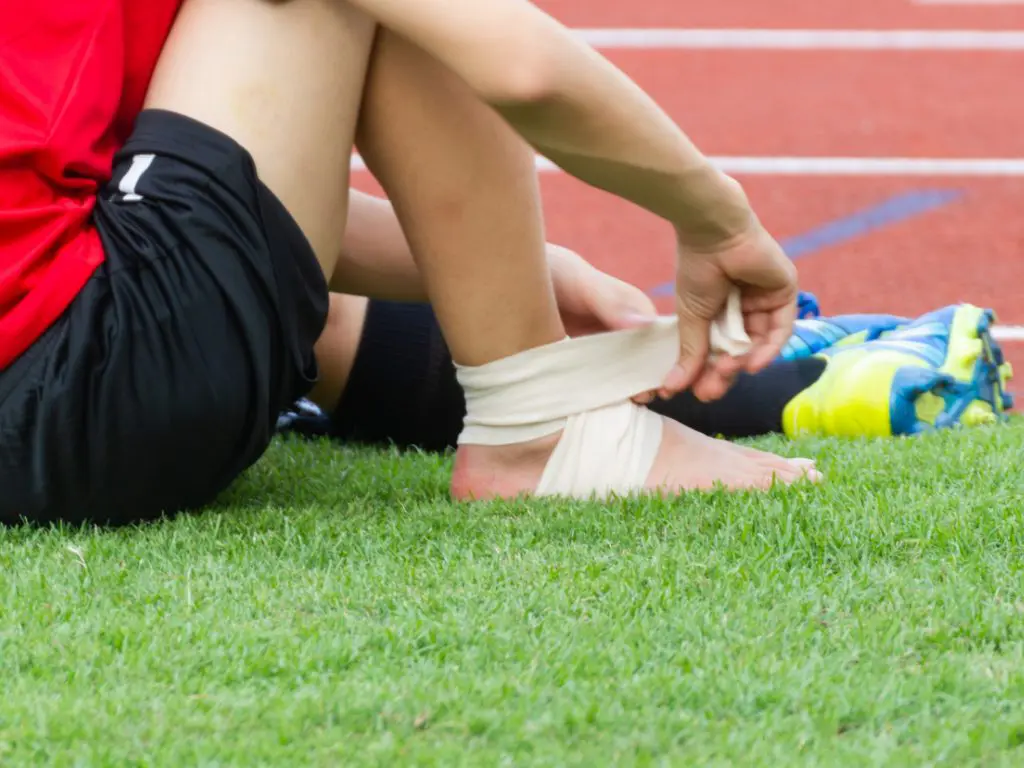 Athlete sitting on the ground before the game starts so he can wrap an ankle support around his ankle.