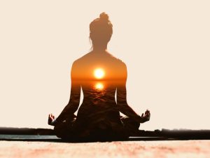 A serene silhouette of a woman meditating at sunrise, symbolizing the mental and emotional benefits of yoga for well-being and balance.