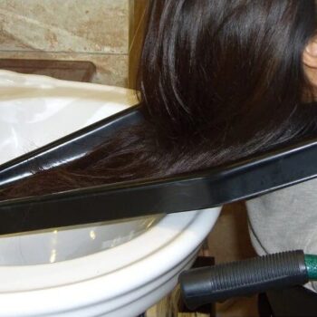 Woman using a black hair wash tray positioned between her neck and a sink, showing how the tray directs water safely into the basin