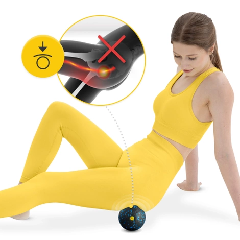 Woman in a yellow workout outfit using a black and blue speckled massage ball under her thigh, with an inset graphic showing joint pain relie
