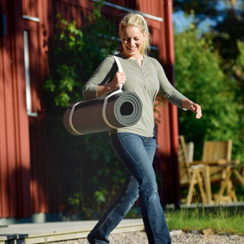 Woman using the SISSEL Yoga and Pilates Mat Carry Strap to carry a rolled-up yoga mat over her shoulder