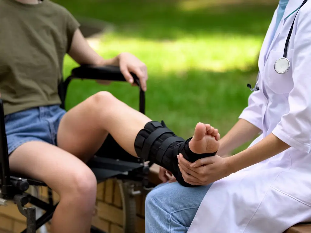 Injured young girl sitting on a wheelchair in her garden using a ankle support to help her ankle heal faster.