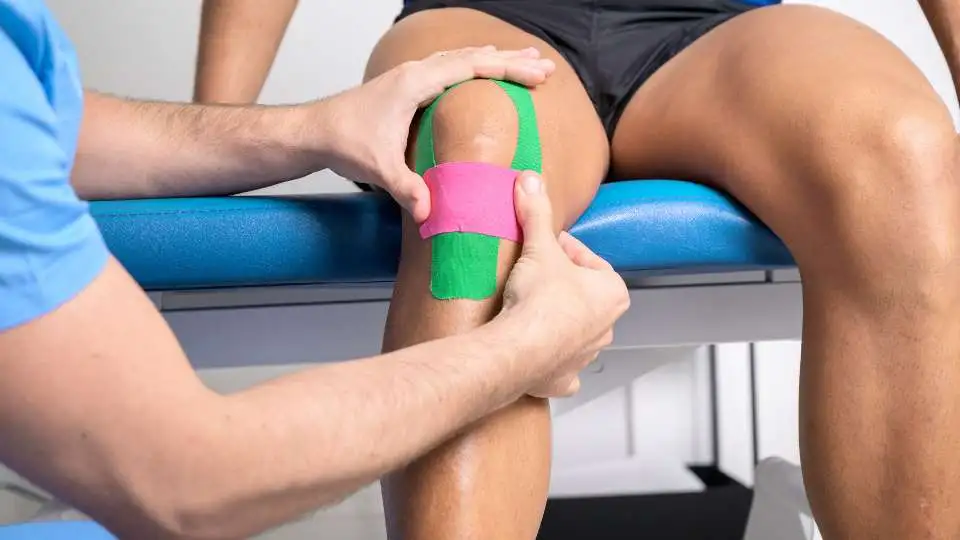 Doctor places pink kinesio tape on a athletes' knee.